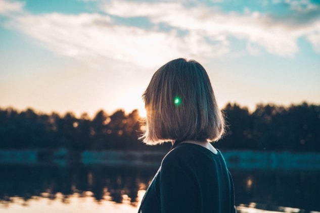 Woman with head turned to the camera looking at the sunset over a lake.