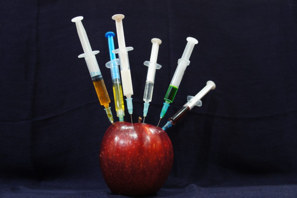 Syringes sticking out of a red apple.