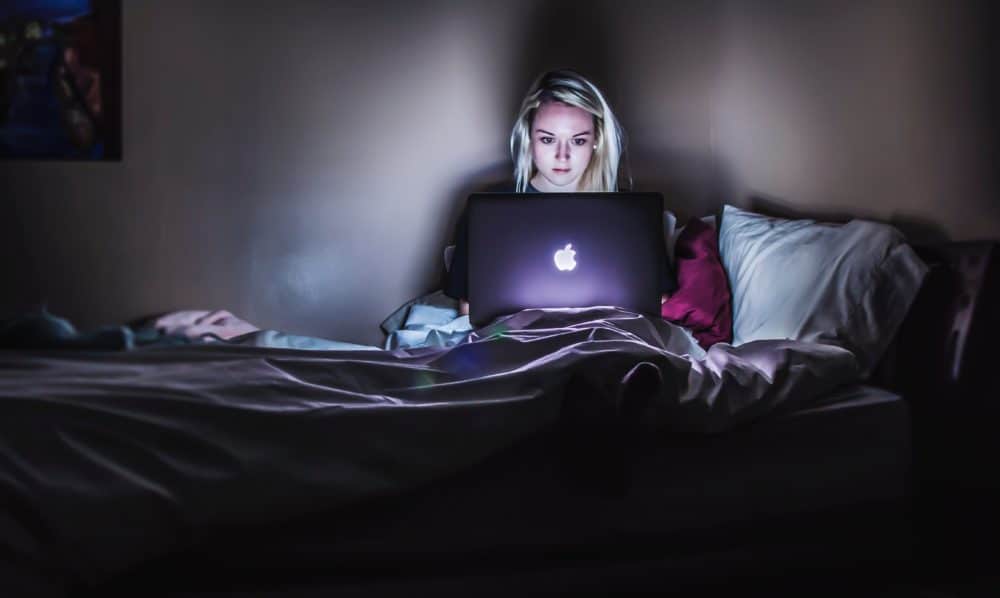 Woman in a dark room looking at laptop in bed.