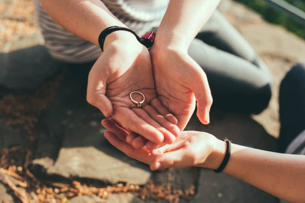 Two people cupping hands around a ring while sitting outside.