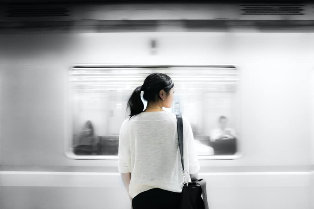 Woman with back turned to camera standing in front of a passing subway car.