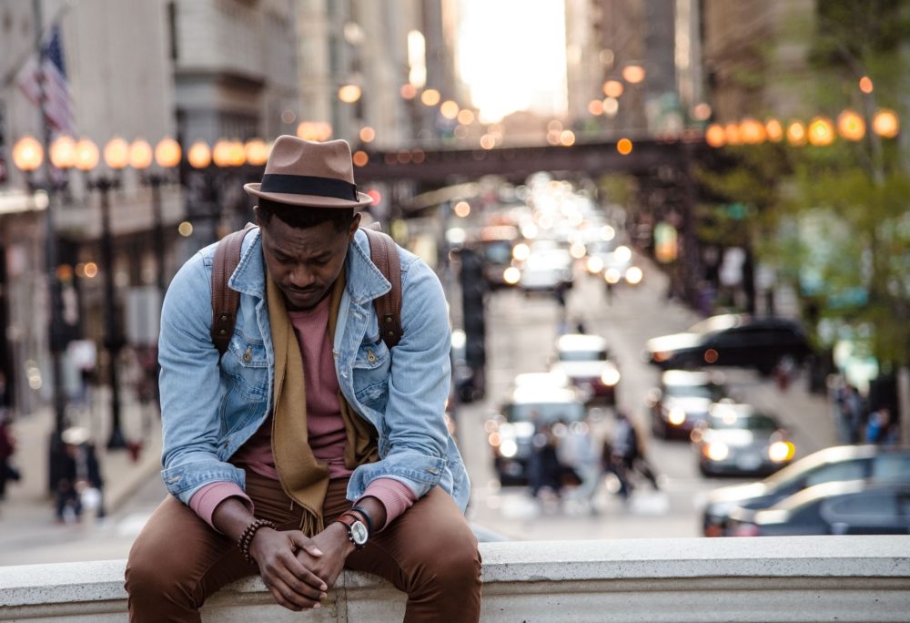 Man sitting on wall with blurred city street behind him.