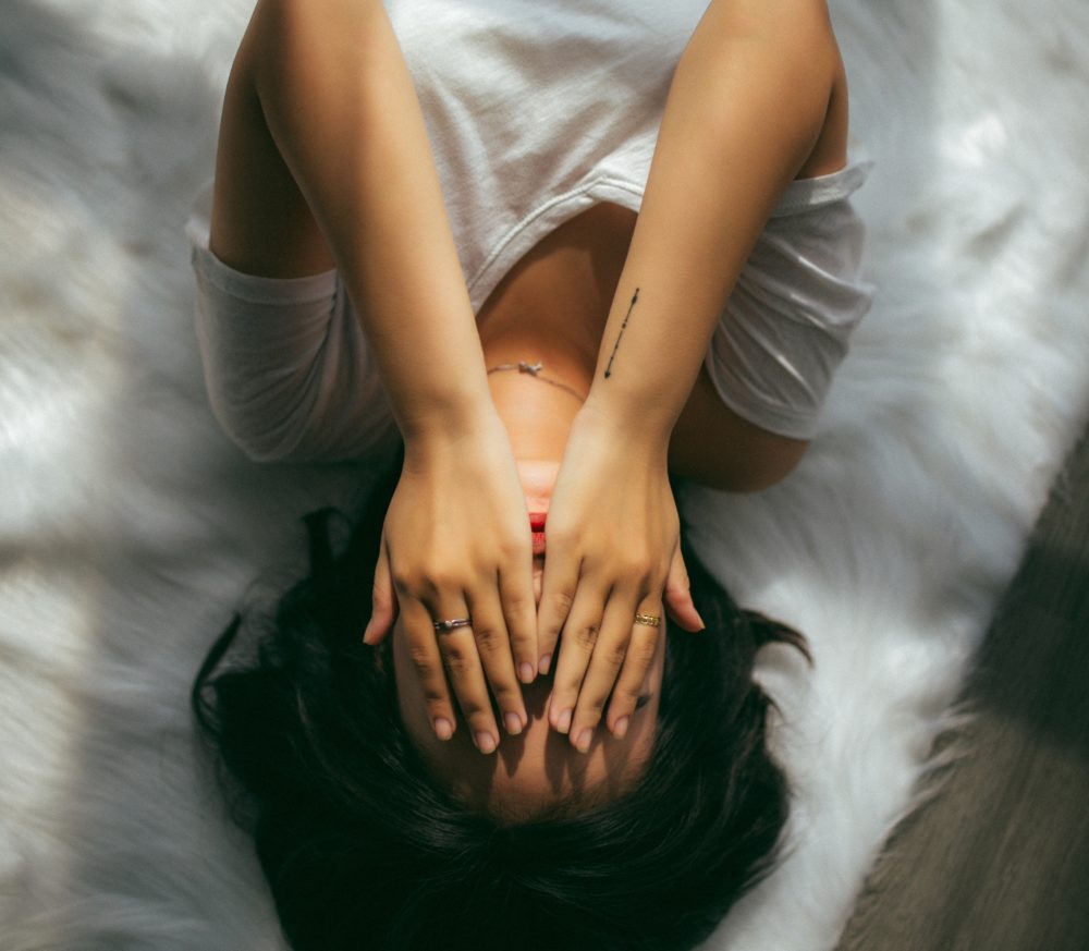 Woman lying on bed with hands covering face.