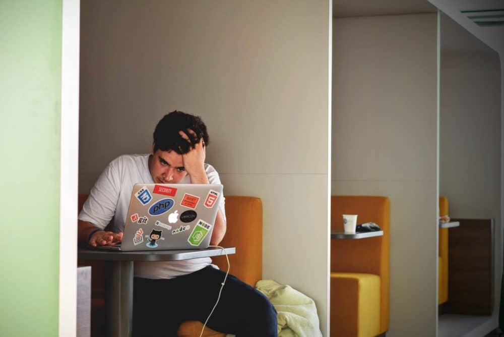 Man in booth with hand in his hair looking at laptop.