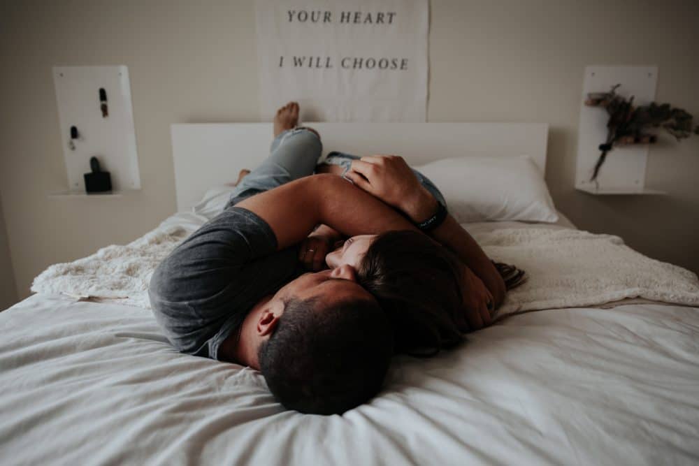 Couple embracing while lying on bed and banner reading "your heart I will choose" at head of bed.