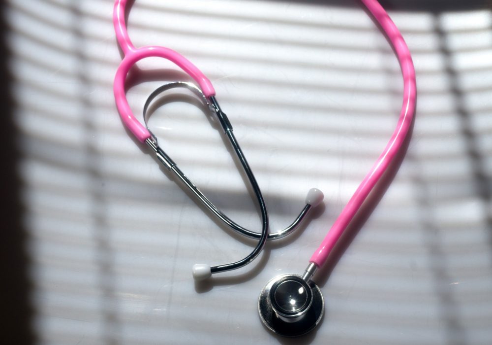 Pink stethoscope on white background with shadows.