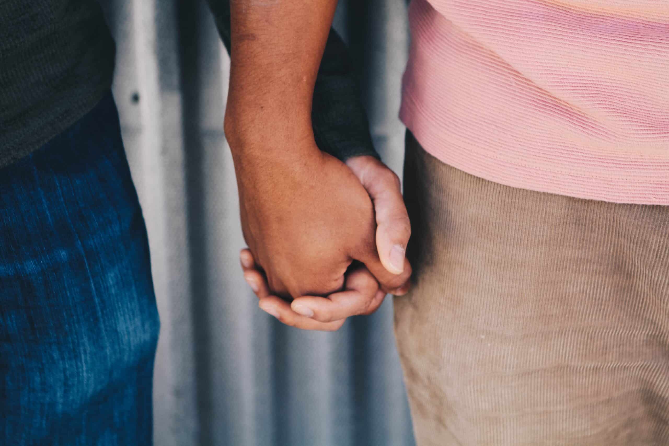 Close-up of two men holding hands.