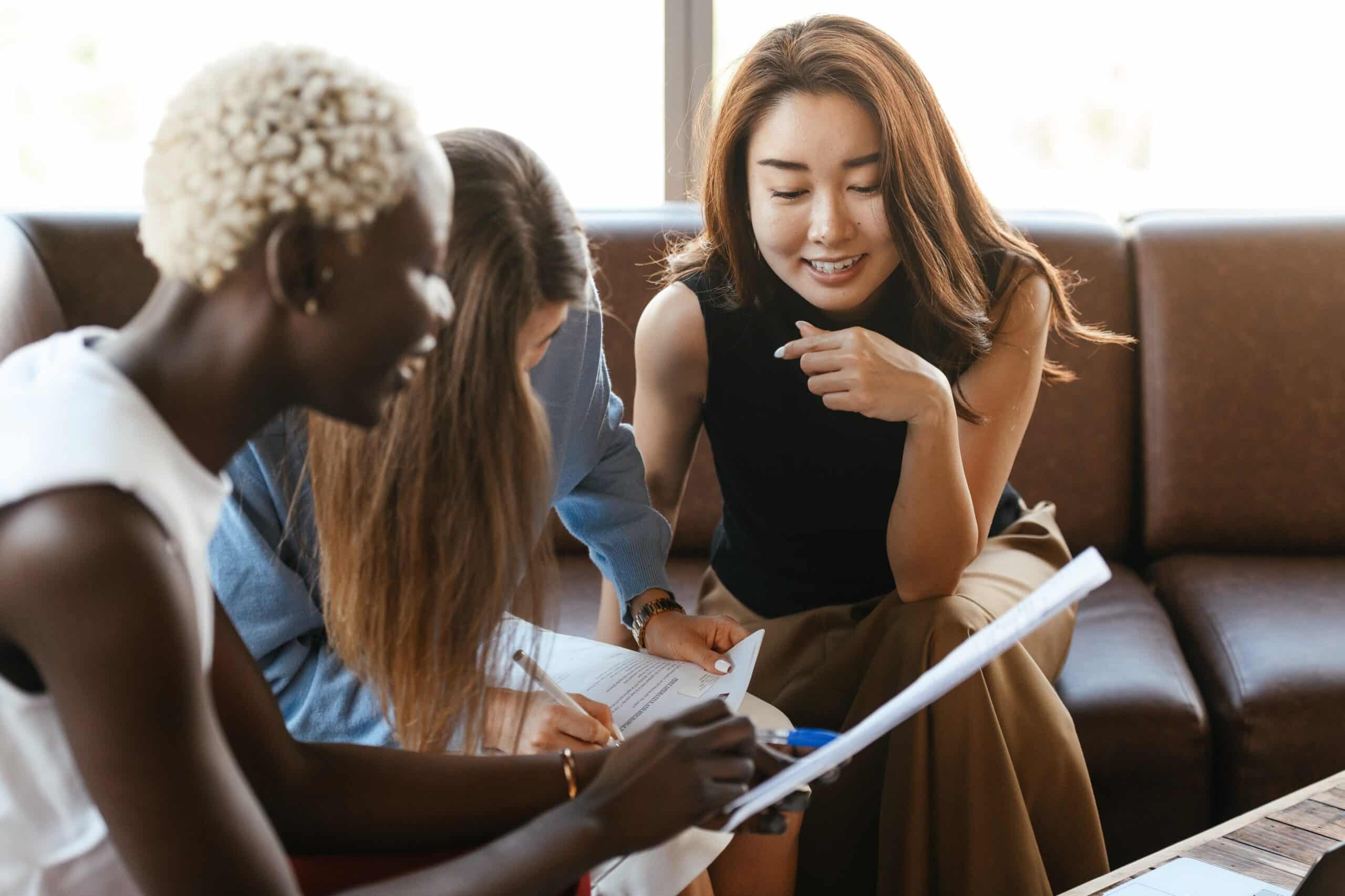 Three women talking and looking at papers.