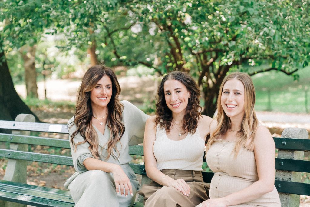 Cofertility Co-founders sit on a bench together and smile.