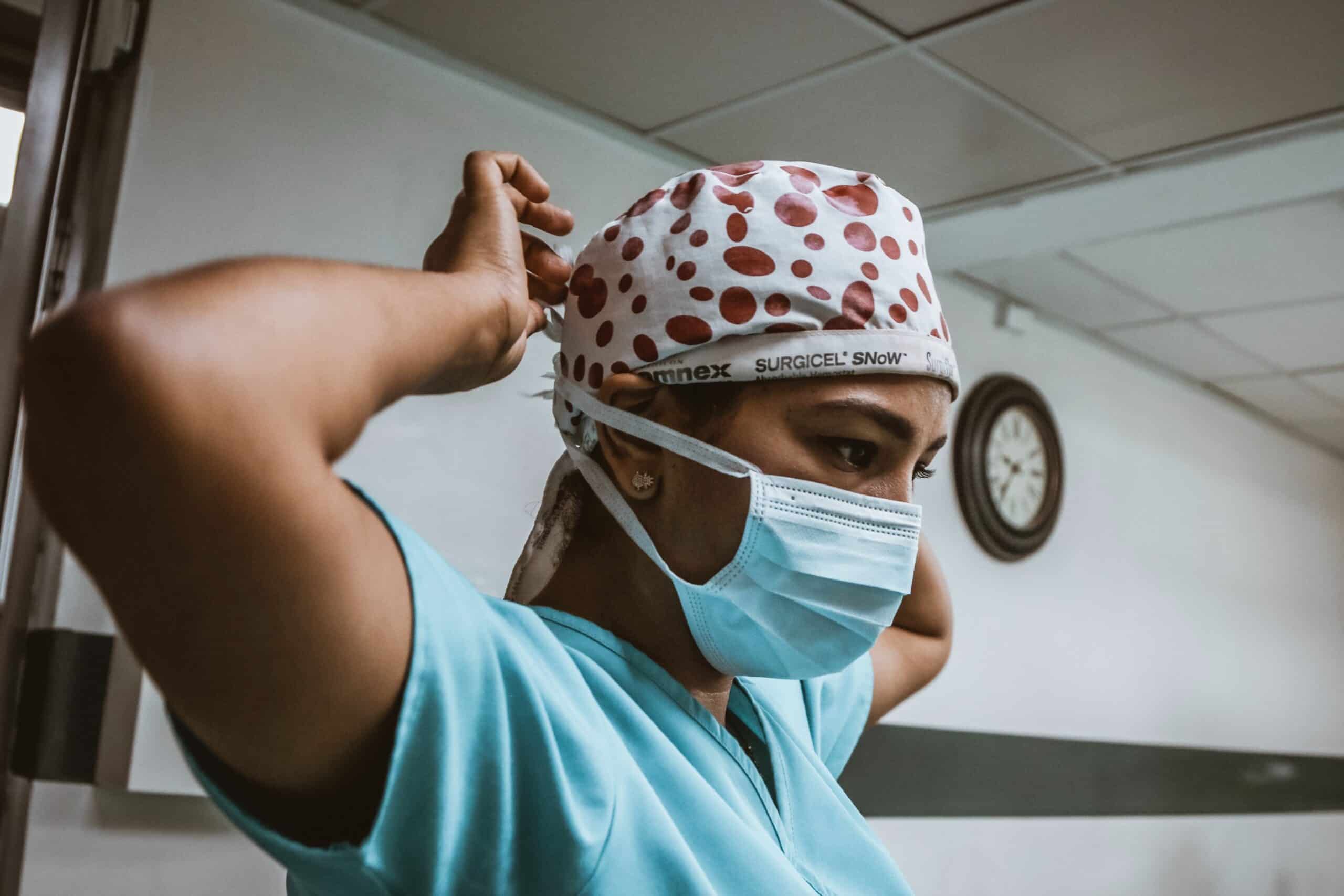 Person wearing scrubs tying on their mask.