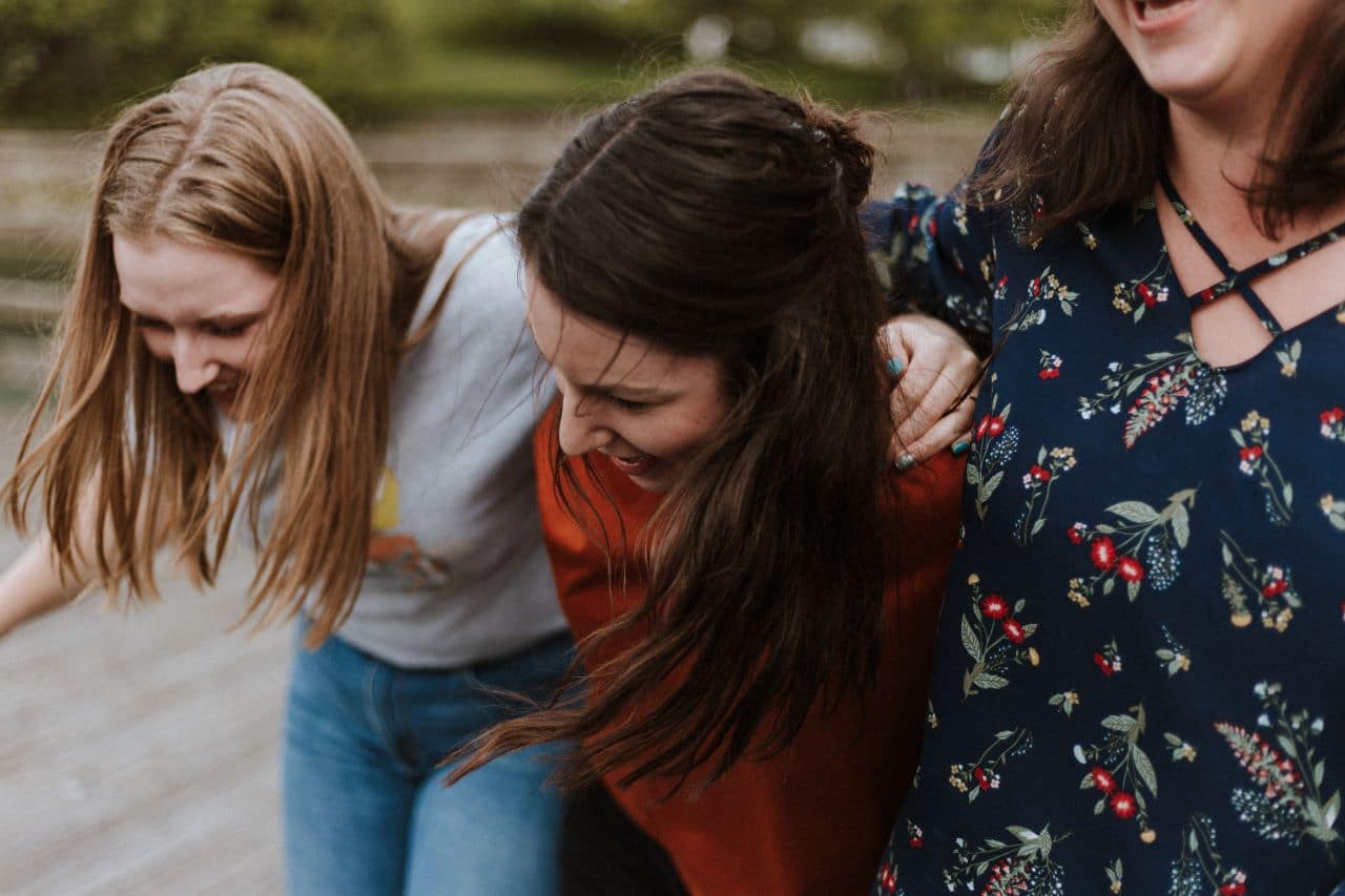 Three women walking with arms around each other's shoulders.
