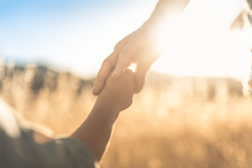 A child holds a parent's hand with the sun in the background.