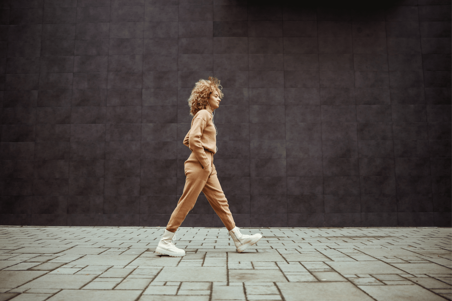 Woman walking down a sidewalk with headphones.
