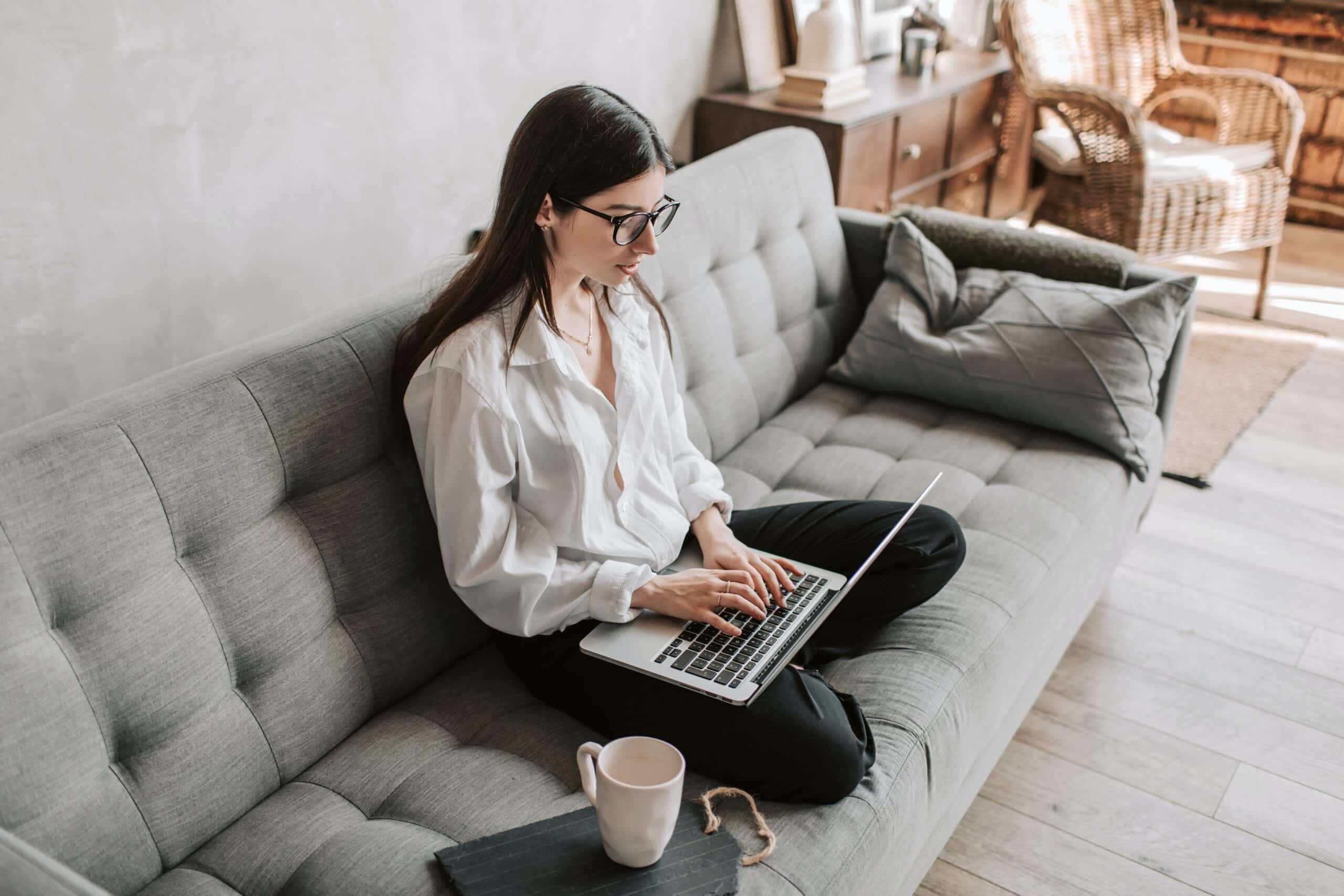 Woman sits on sofa typing on laptop.