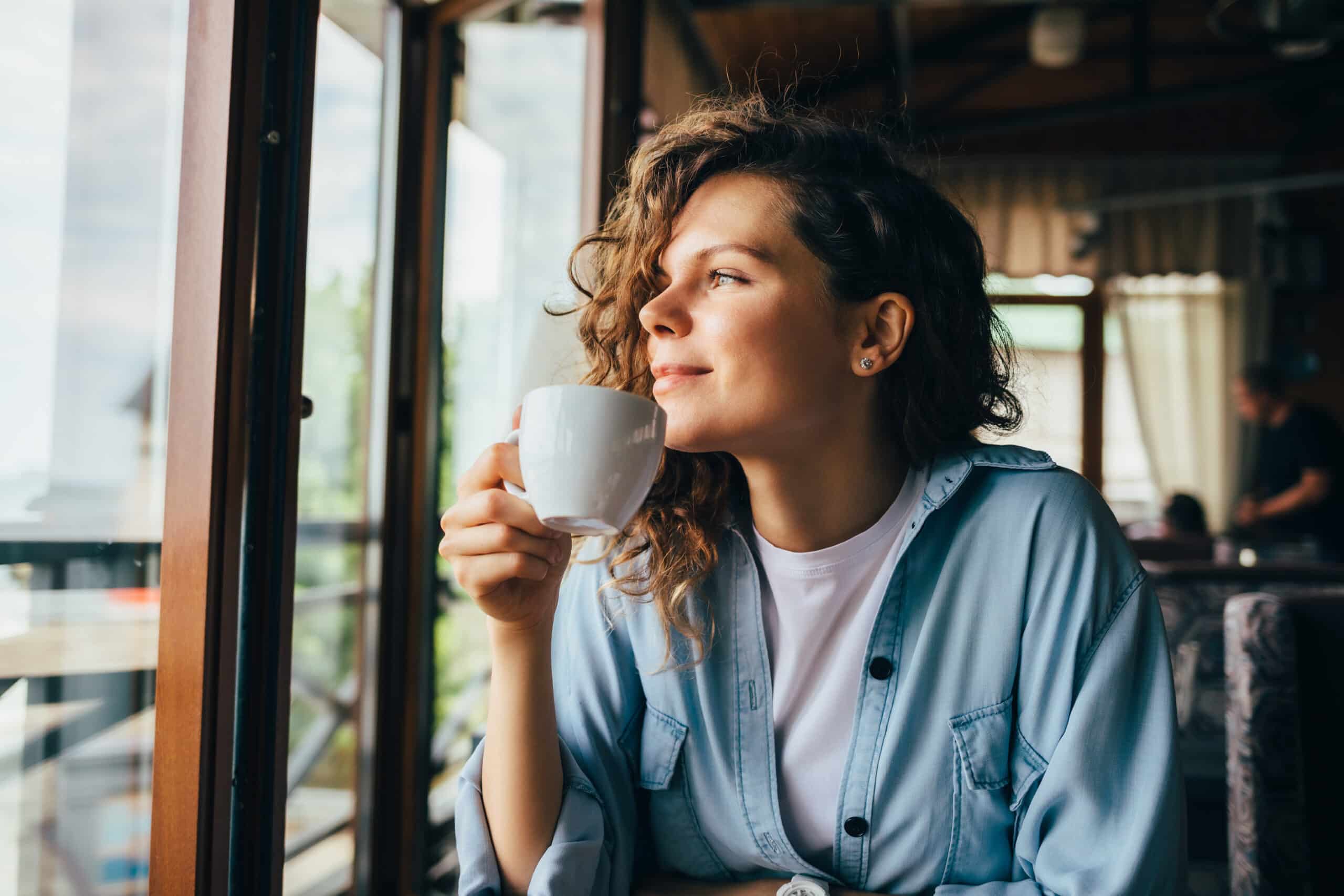 Woman in a coffee shop sitting at a table next to a window