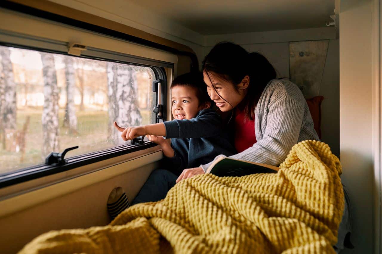 Woman and child under blanket looking out a window.