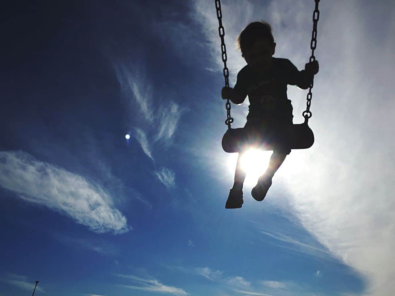 Young boy on swing with blue sky and clouds behind him.