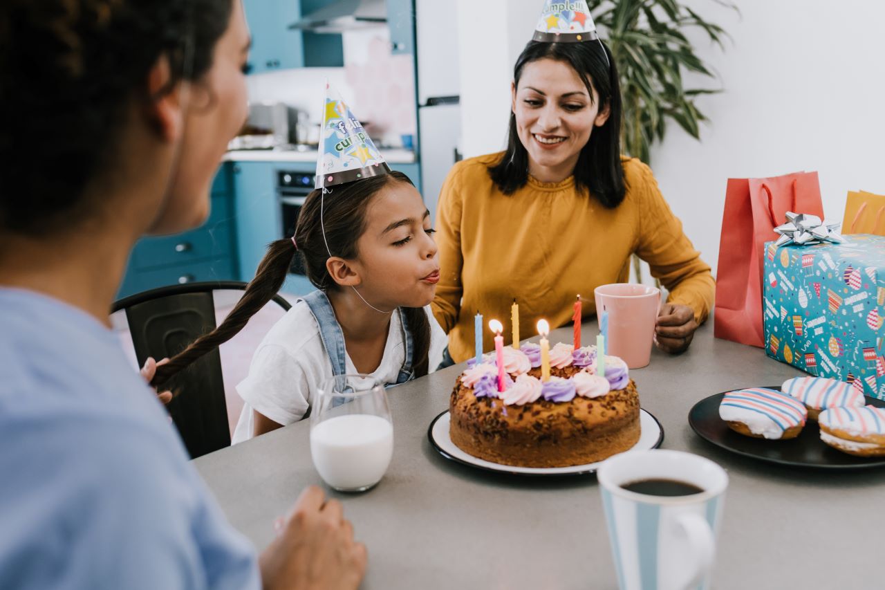Woman watching girl blow out birthday candles on a cake.