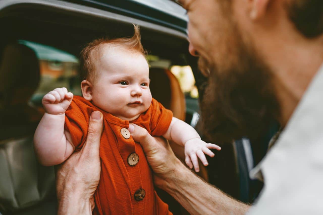 Man holding up baby outside of a car.
