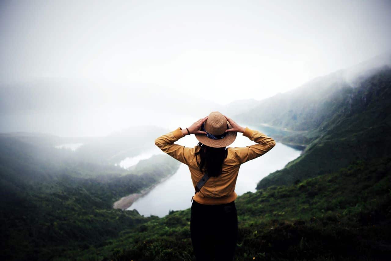 Woman holding hat looking out over a foggy valley.