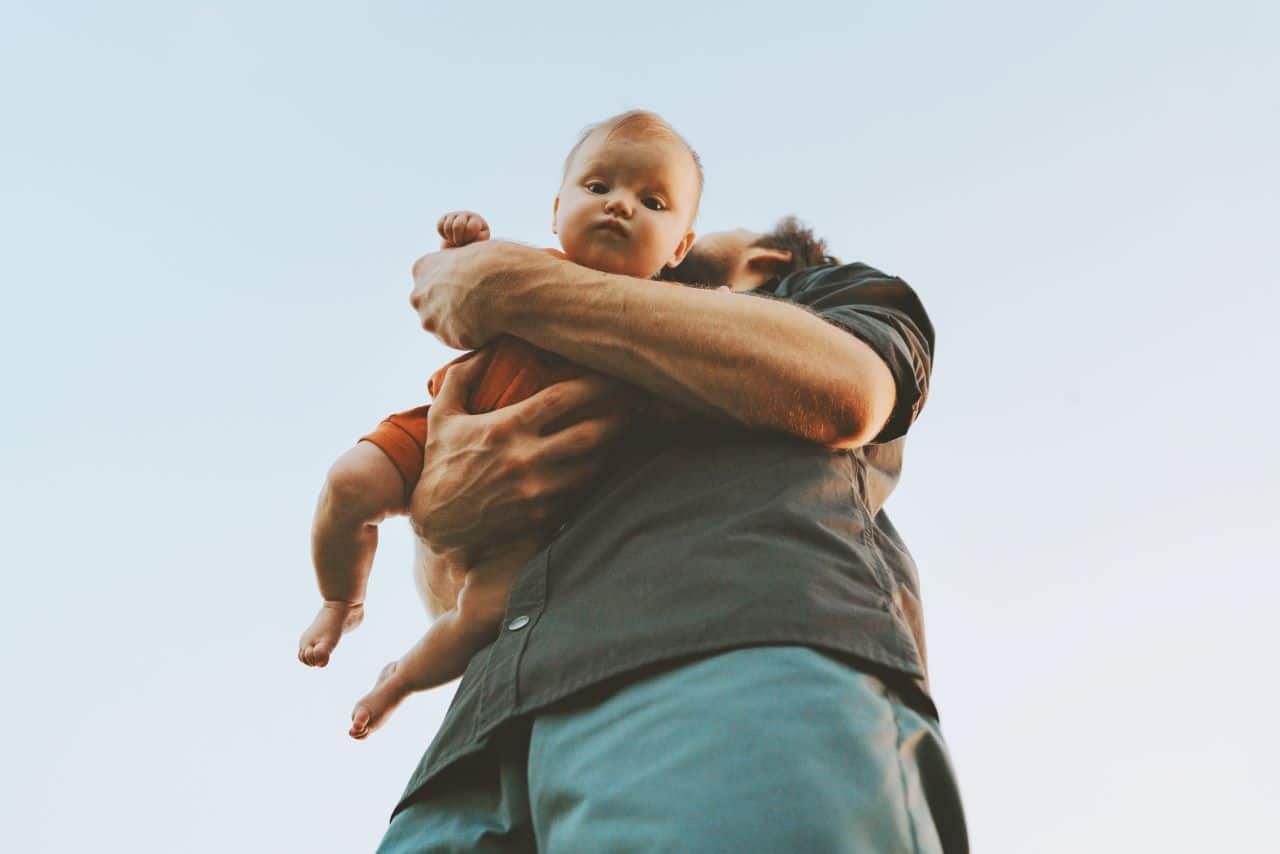 Baby looking down over camera while laying in a man's arms.