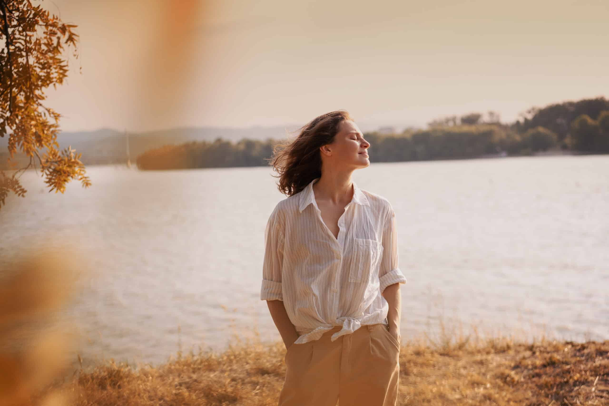 Woman standing in front of a lake looking to her left and smiling.