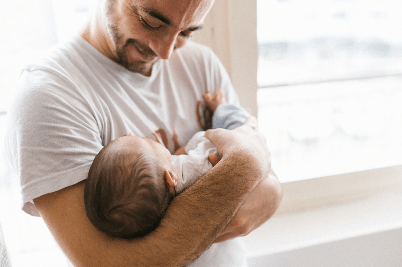 Man looking down at a baby in his arms.