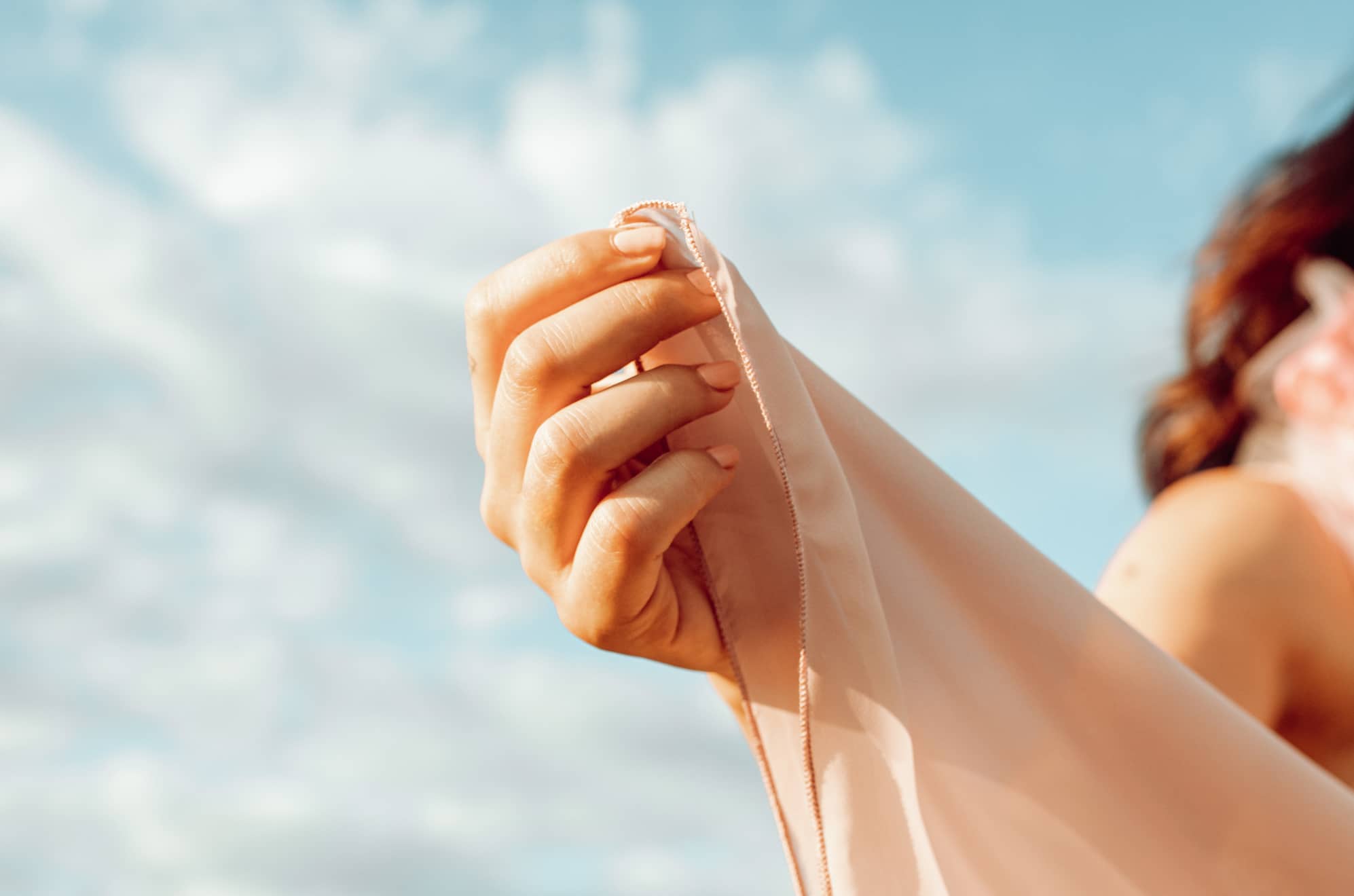 A female hand delicately holding a sheer fabric in an outdoor setting.