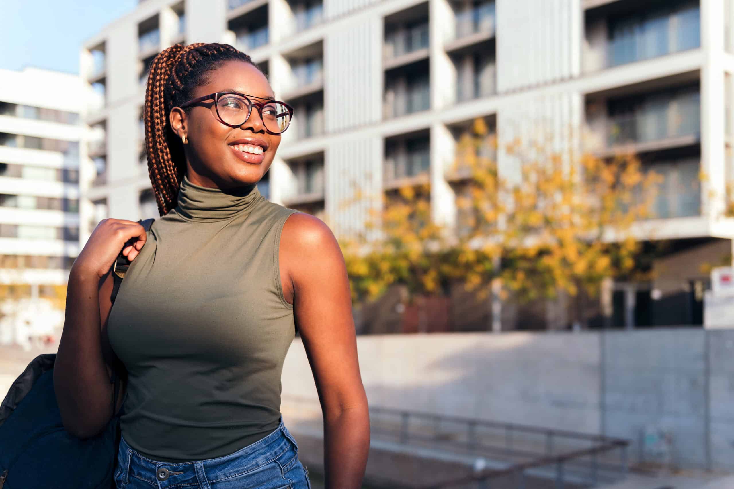 a woman with dark skin and long braided hair looking into the distance while standing outside in a city