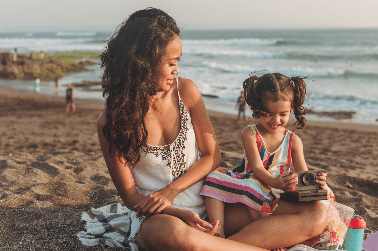 an image of a mother and daughter sitting on a blanket at the beach
