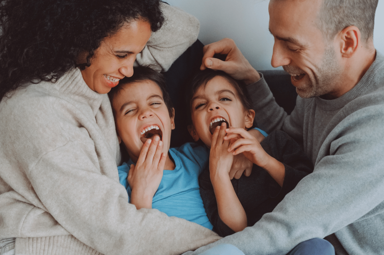 a mother and father snuggle with their laughing children on a bed