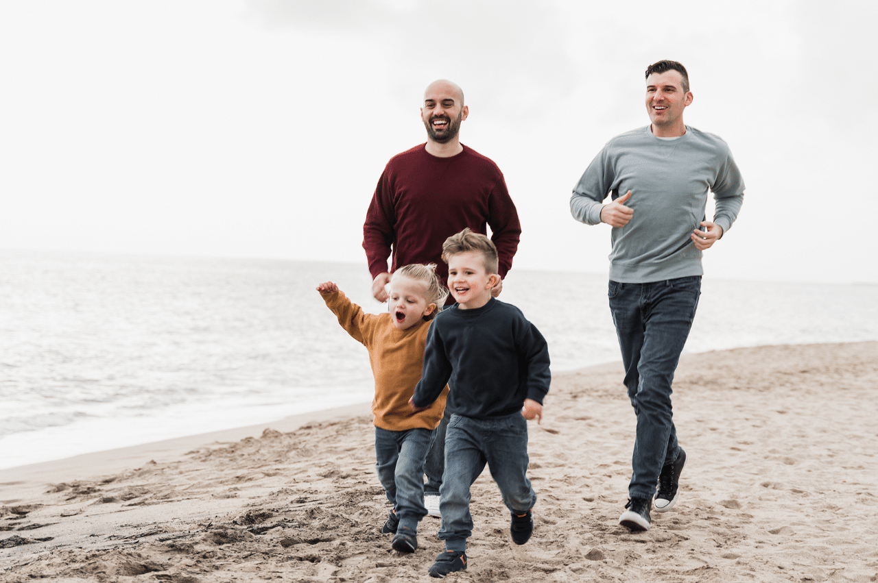 two gay dads running behind their children on the beach