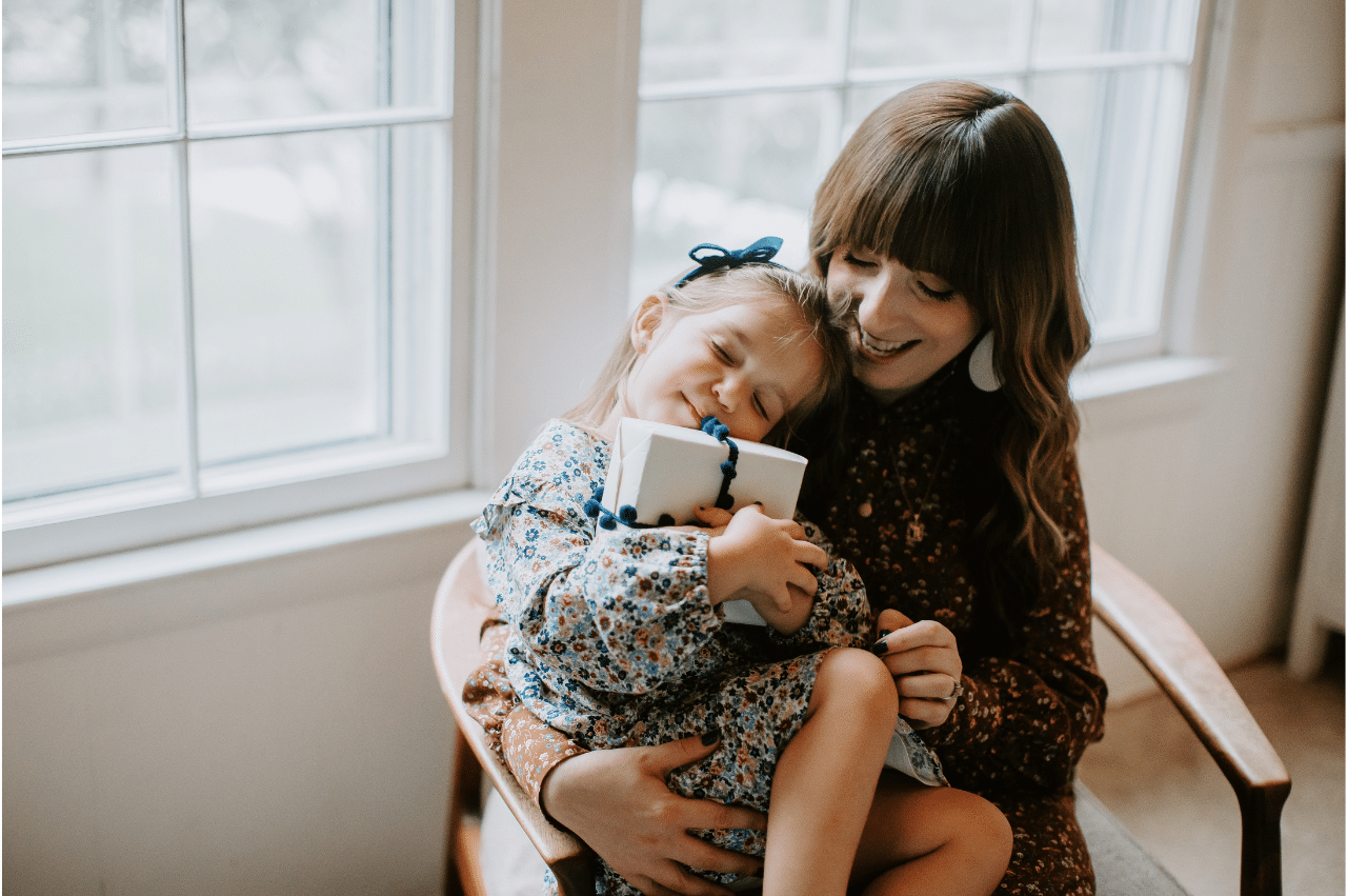 a mother and her young daughter sitting together on a chair and hugging