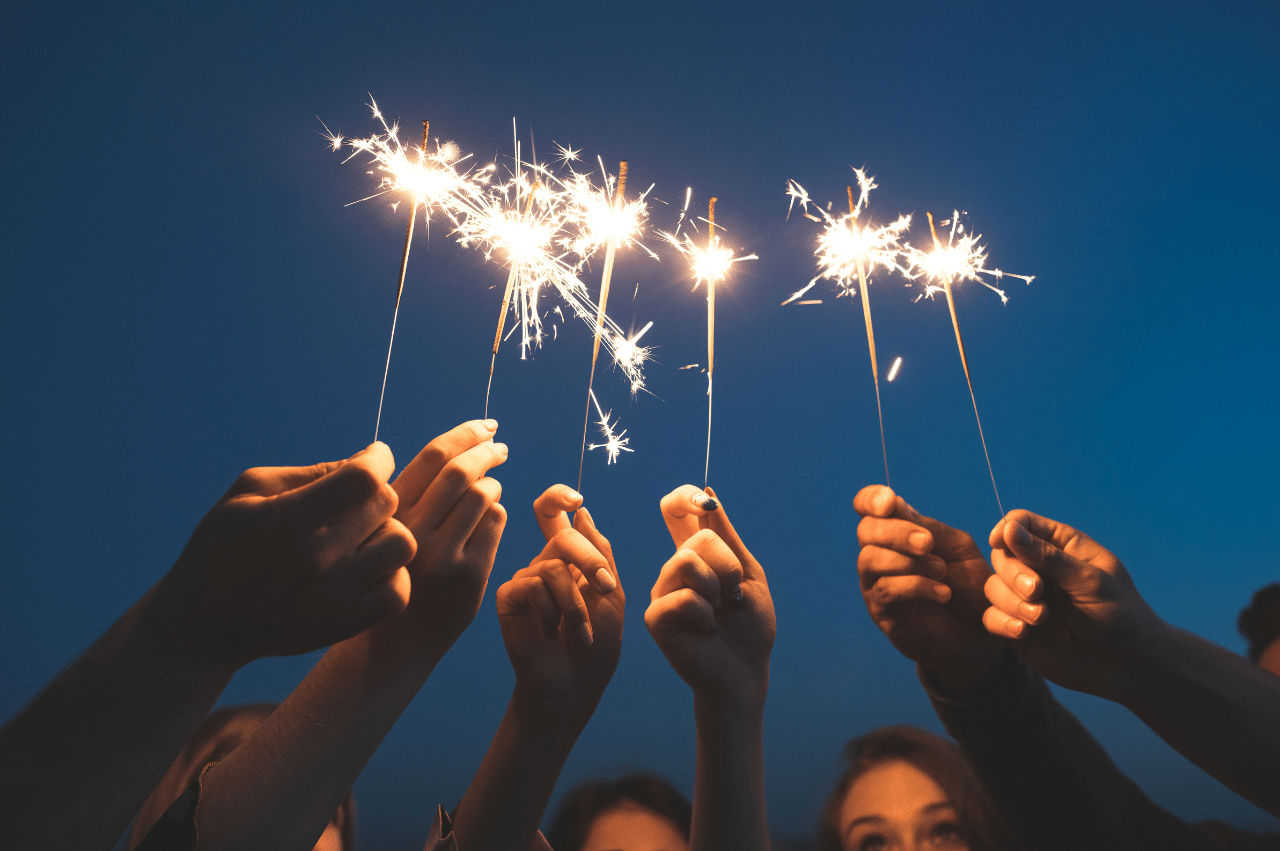 a group of hands holding lit sparklers