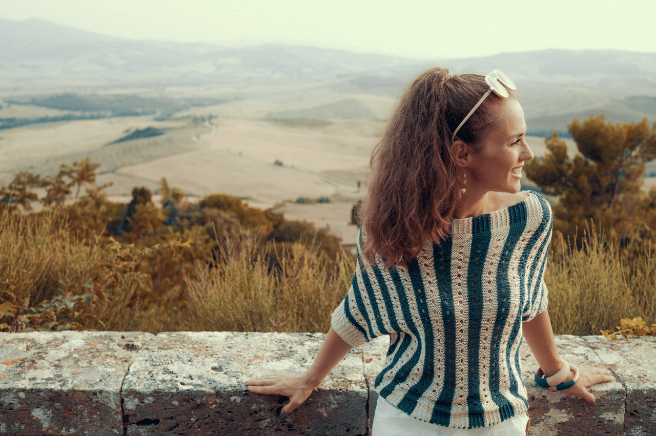 a young woman with her back against a short wall overlooking mountains