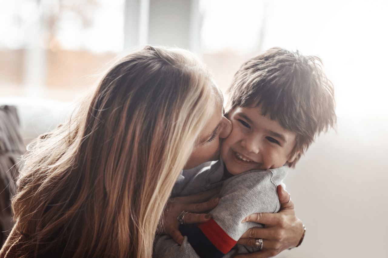 a mom embracing her young male child and kissing him on the cheek