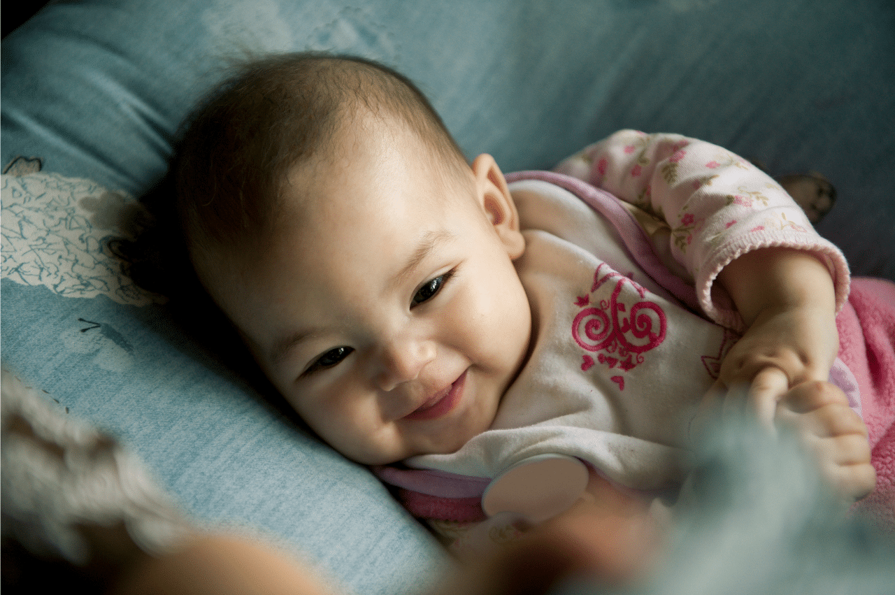a smiling baby laying on a blue pillow and looking up at their parent