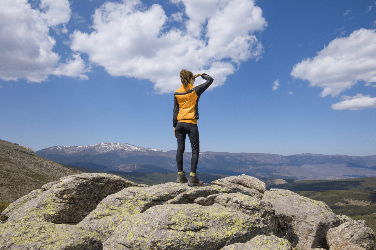 a woman from behind standing on a mountain peak looking out into the distance