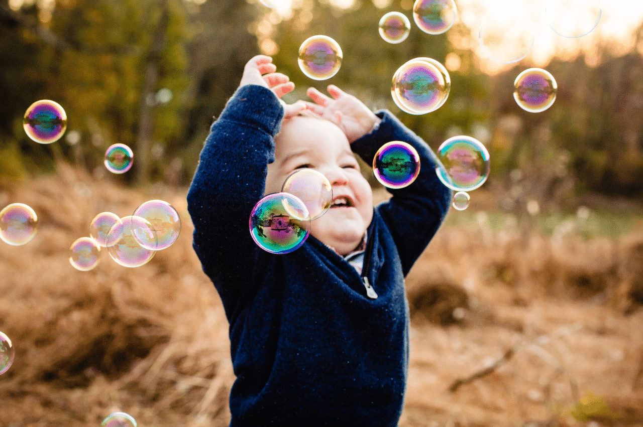 a toddler-aged boy in a grassy field playing with bubbles