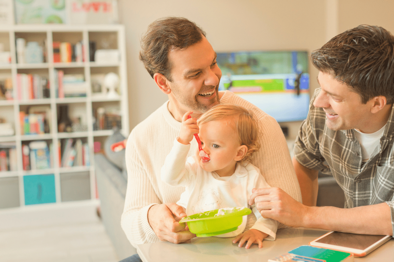 a gay male couple sitting at a table feeding their young child