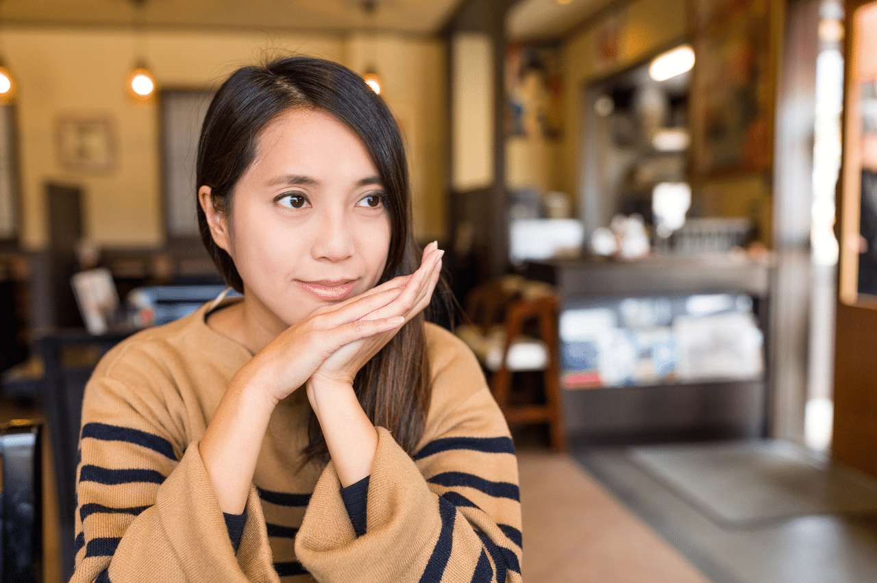 a young asian woman sitting in a coffee shop setting looking to the distance on her right