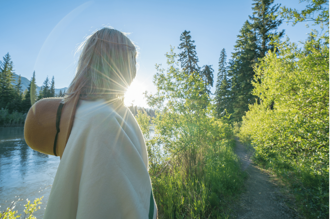 a young woman with blonde hair photographed from behind. she is standing outside with the sun shining brightly in front of her