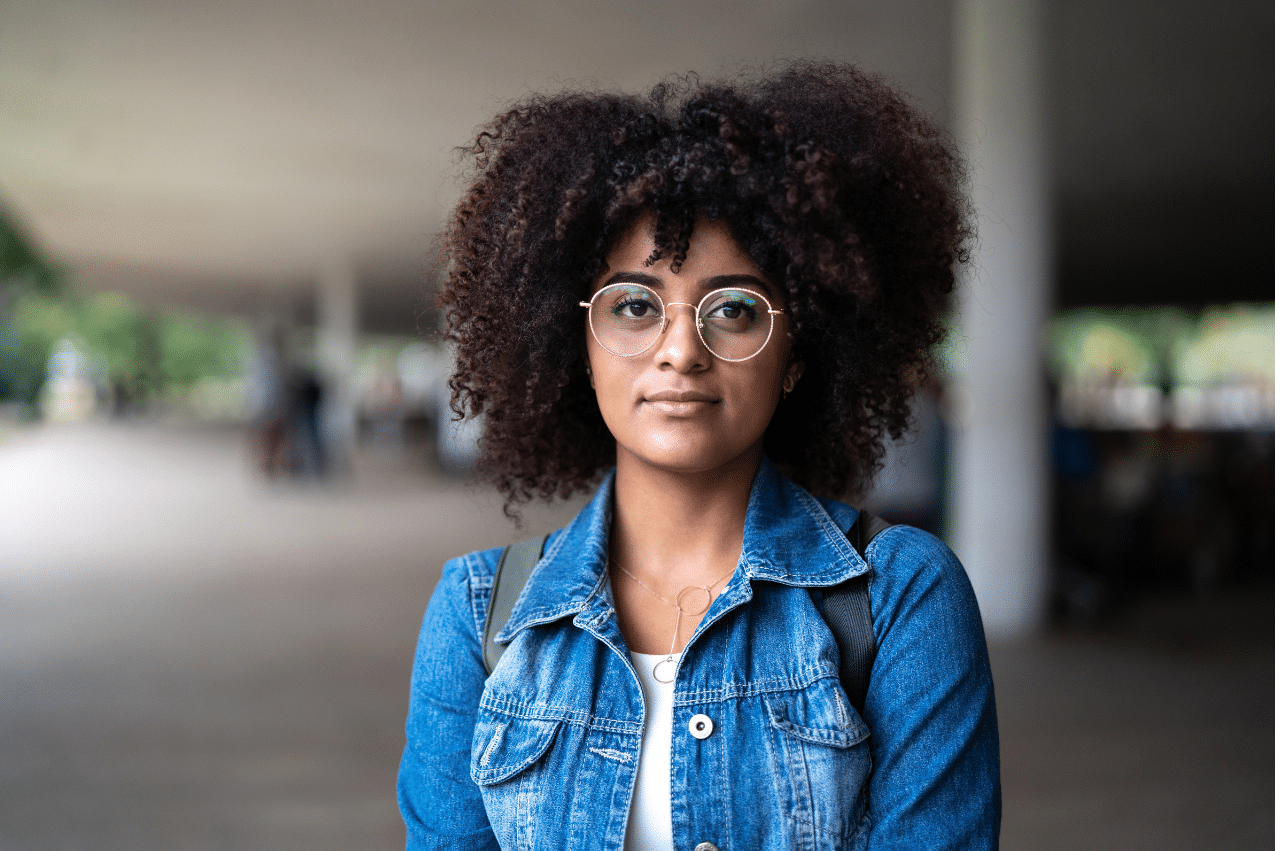 a young woman looking straight into the camera standing outside in a parking garage-like setting