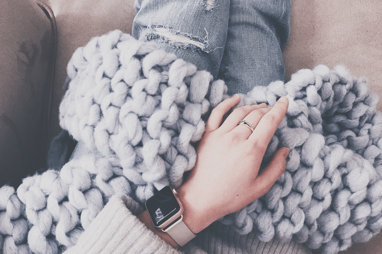 A person's legs sitting on the couch holding a knit blanket