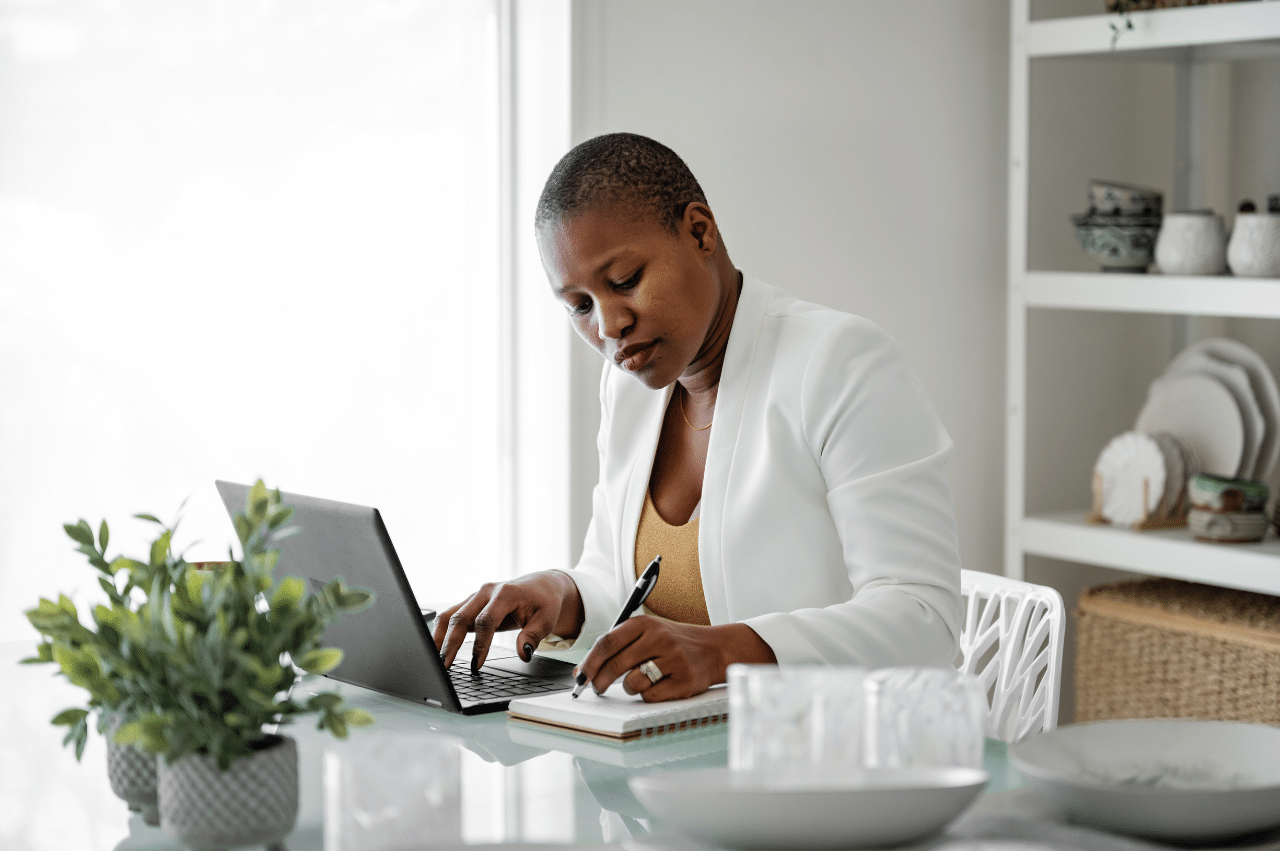 Adult wearing a white blazer sitting at white desk with a laptop
