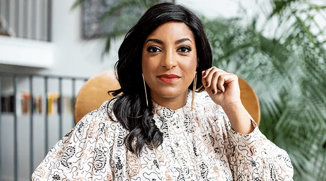 Headshot of a woman smiling. Her left hand is positioned near her face.