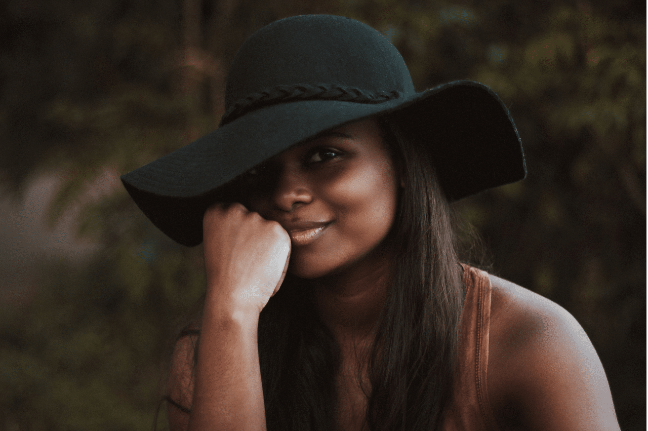 Woman posing with her head rested on her fist. She is wearing a floppy