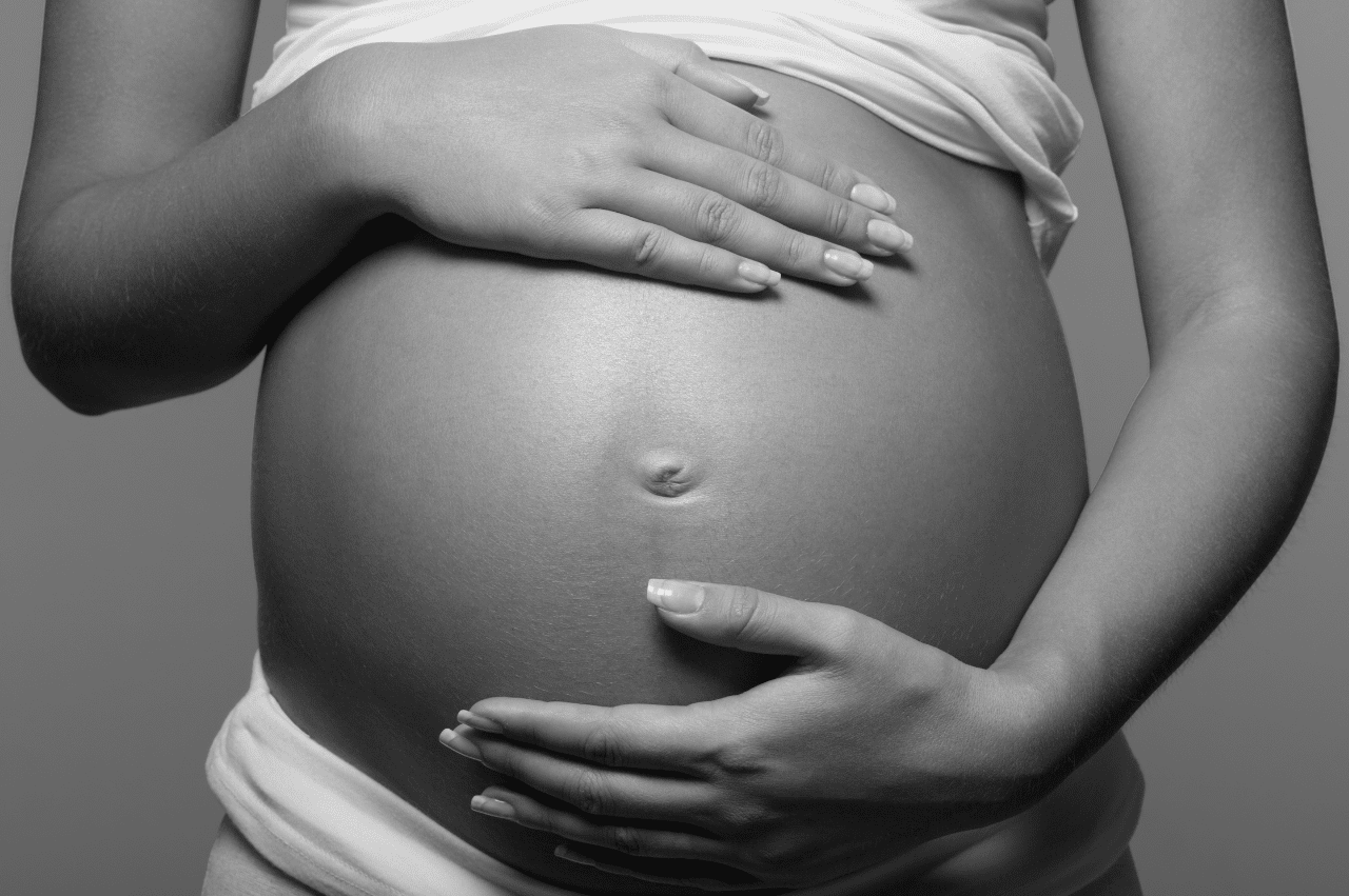 Black and white image of a person holding their pregnant belly