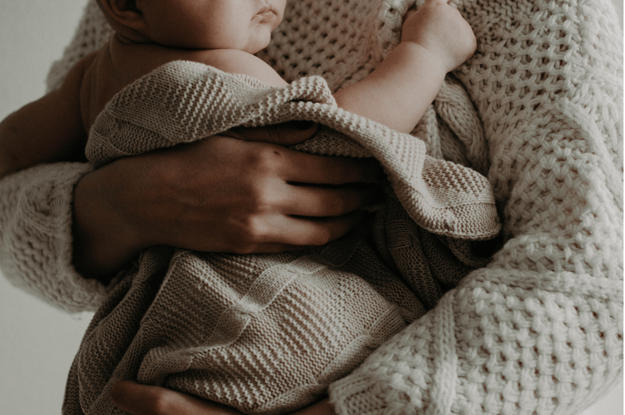 Baby wrapped in a knit blanket being held in someone's arms