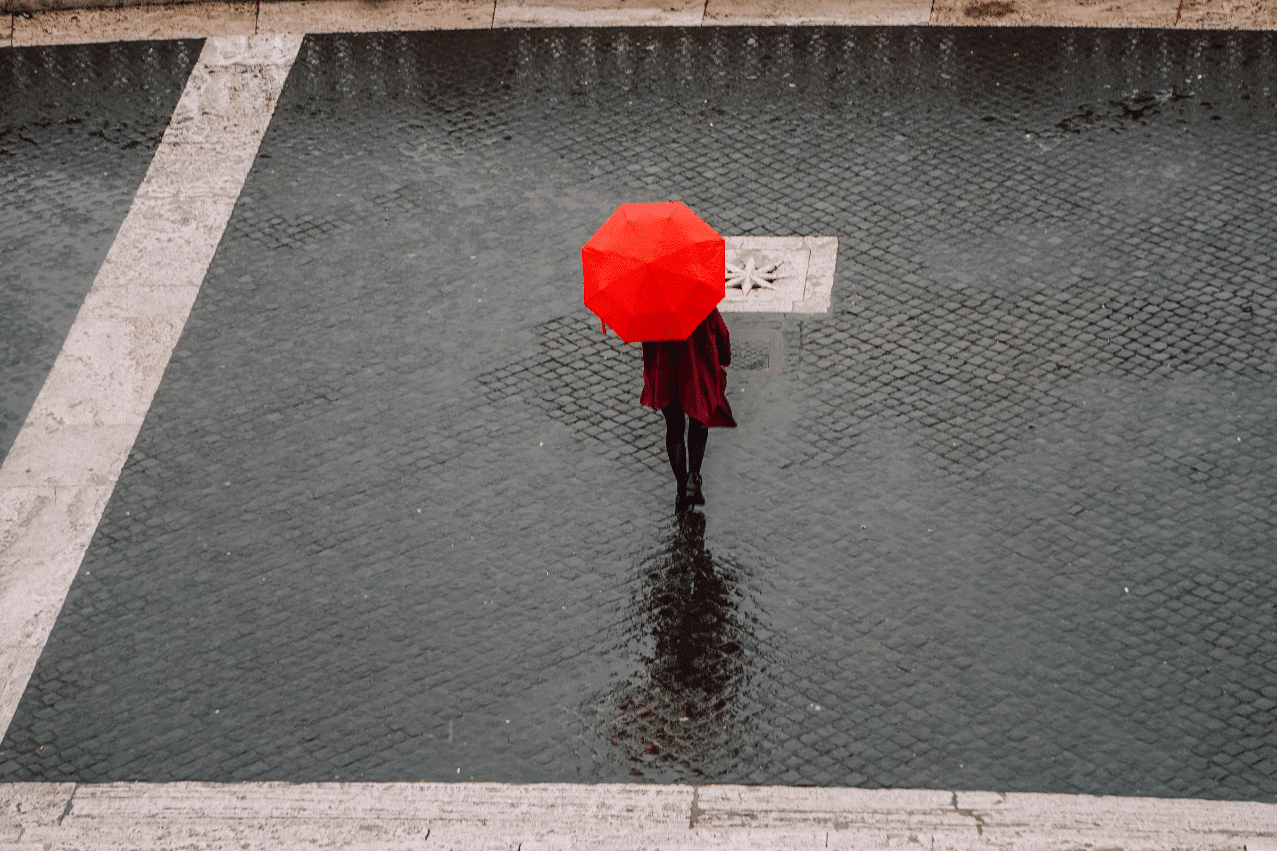 A lone person standing with a red umbrella as it rains